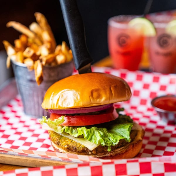 A Burgar burger with fries, ketchup, and two pink drinks with lime on a red and white checkered tray.